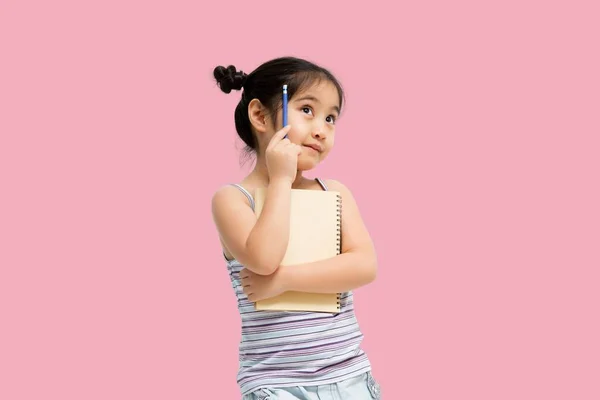 带有复制空间的画像 空旷的地方 一个心事重重的亚洲小女孩 手里拿着纸和铅笔抬头看 作家在等待缪斯 孤零零地躺在粉红的背景上 — 图库照片