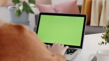 Young Asian woman using laptop computer at home with green blank monitor screen.