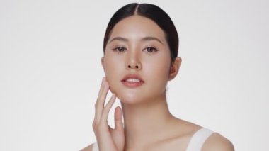 Beauty young Asian woman face looking at camera, isolated on white background. Skin care treatment or cosmetic ads concept. Beautiful female model with perfect fresh and clean skin.