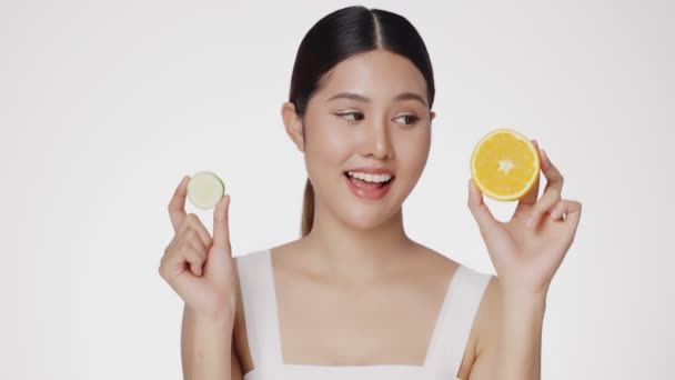 亚洲女人喜欢干净健康的皮肤 可爱的女模洁白新鲜的皮肤上夹着一片黄瓜和橙子 面部表情的表达 — 图库视频影像