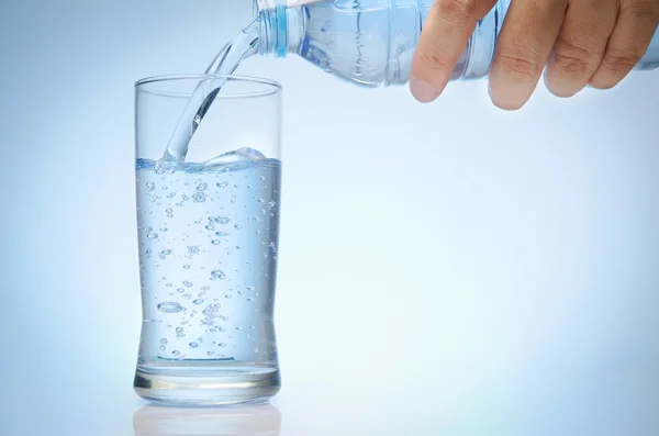 Reines Wasser wird in ein Glas Wasser aus der Flasche entleert — Stockfoto