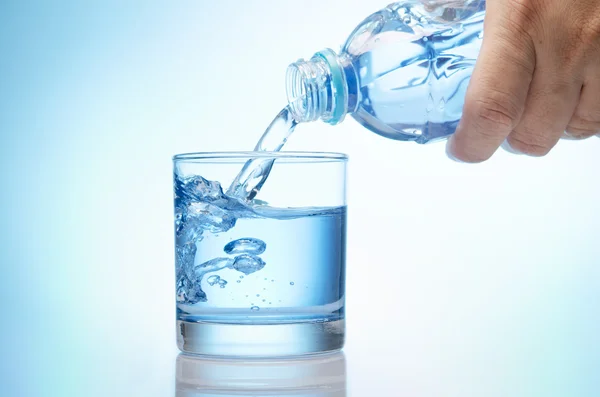 Reines Wasser wird in ein Glas Wasser aus der Flasche entleert — Stockfoto