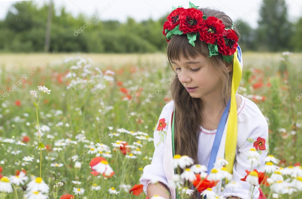 Little girl in Ukrainian national costume collect wild flowers