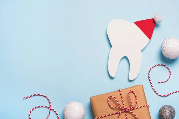 Yılbaşı ve yeni yıl diş hekimliği geçmişi. Kırmızı Noel Baba şapkası, hediye ve şenlikli süsleme takılı dekoratif diş. Yaratıcı tıbbi kış tebrik kartı. Üst görünüm, kopyalama alanı, düz uzanma