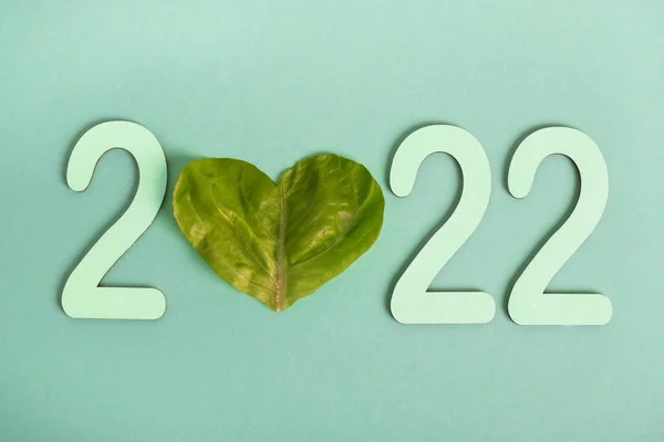 Healthy New Year 2022. Concept of planning balanced eating, diet. Lettuce leaf heart shaped with numbers 2022 on green background. Top view, flat lay