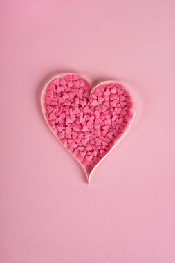 Sevgililer Günü kompozisyonu. Pastel pembe arka planda kalp şeklinde tatlı konfeti. Üst görünüm, düz görünüm, dikey