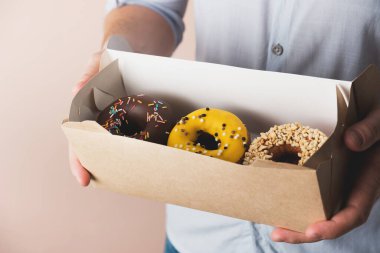 Elinde renkli çöreklerle karton kutu tutan bir adam. Lezzetli tatlı, yemek teslimatı. Yakın çekim.