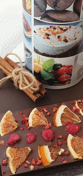 Handmade chocolate with raspberry and orange. Cinnamon sticks and a jar of coffee on the table. Chocolate bar. Sweet dessert.