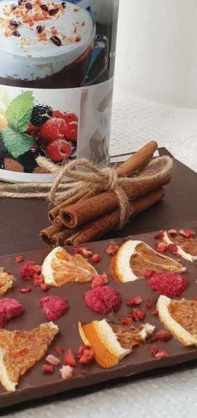 Handmade chocolate with raspberry and orange. Cinnamon sticks and a jar of coffee on the table. Chocolate bar. Sweet dessert.