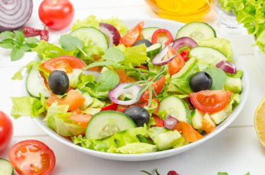 Sağlıklı taze sebze salatası, domatesler, salatalıklar ve dolmalık biberler beyaz ahşap bir arka planda..