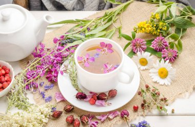 Biberli bitki çayı, papatya çayı ve yonca beyaz bir fincanda çiçekli ahşap bir masada.
