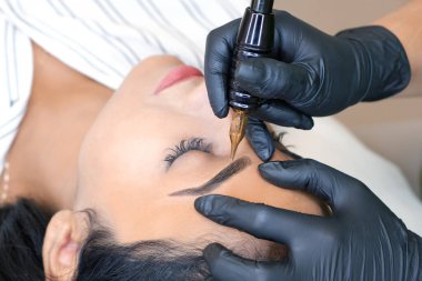 Güzellik uzmanı genç ve güzel bir kadının yüzüne kalıcı kaş makyajı yapar.