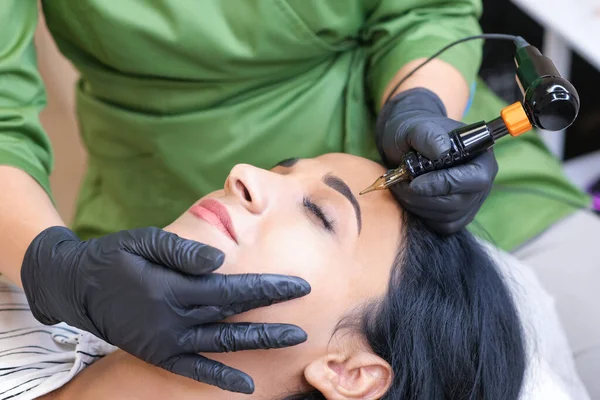 Güzellik uzmanı genç ve güzel bir kadının yüzüne kalıcı kaş makyajı yapar.