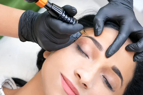 Güzellik uzmanı genç ve güzel bir kadının yüzüne kalıcı kaş makyajı yapar.