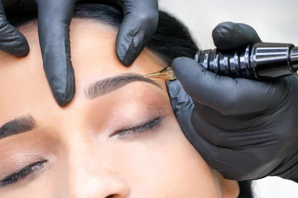 Güzellik uzmanı genç ve güzel bir kadının yüzüne kalıcı kaş makyajı yapar.