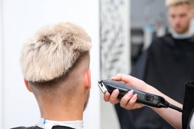 Berber salonundaki koltukta saç kesme makineli sarışın genç adamın saç kesimi, erkekler ve çocuklar için berber dükkanı konsepti