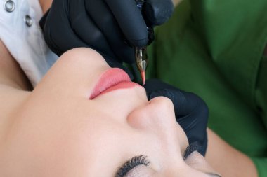 Güzellik salonunda dudaklarında kalıcı makyaj yapan genç bir kadın. Doğal yeşil arkaplan