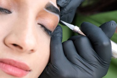 Güzellik uzmanı genç ve güzel bir kadının yüzüne kalıcı kaş makyajı yapar.