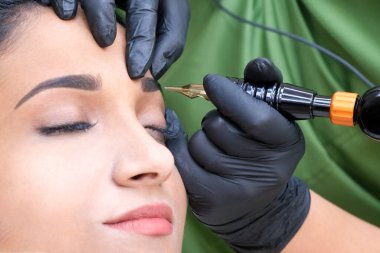 Güzellik uzmanı genç ve güzel bir kadının yüzüne kalıcı kaş makyajı yapar.