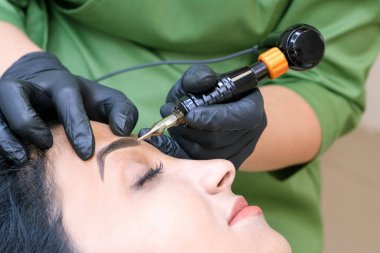 Güzellik uzmanı genç ve güzel bir kadının yüzüne kalıcı kaş makyajı yapar.