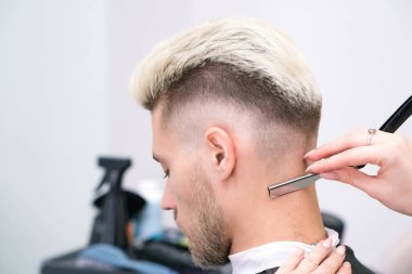Jilet gibi keskin. Berber salonundaki sarışın genç adamın saç kesimi, erkekler ve oğlanlar için berber dükkanı konsepti