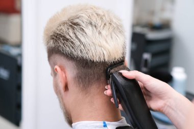 Berber salonundaki koltukta saç kesme makineli sarışın genç adamın saç kesimi, erkekler ve çocuklar için berber dükkanı konsepti
