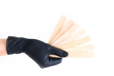 Siyah bir eldiven, beyaz izole arka planda tüy dökmek için tahta çubuklar tutar.