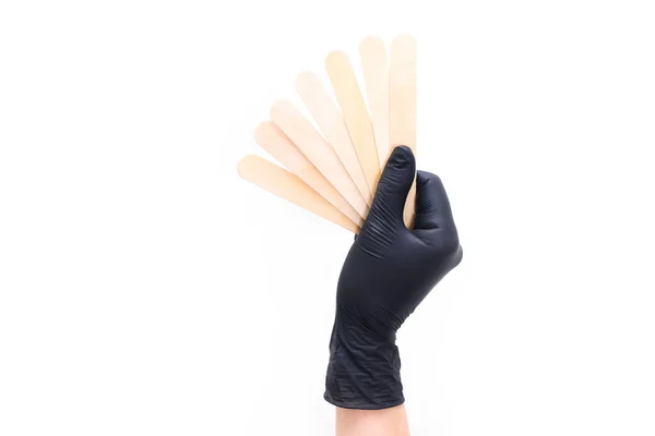 Χέρι Μαύρο Γάντι Κρατά Ξύλινα Ραβδιά Για Αποτρίχωση Λευκό Απομονωμένο — Φωτογραφία Αρχείου