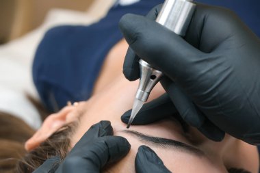 Güzellik uzmanı genç ve güzel bir kadının yüzüne kalıcı kaş makyajı yapar. Kalıcı kaş dövmesi..