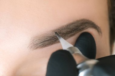 Güzellik uzmanı genç ve güzel bir kadının yüzüne kalıcı kaş makyajı yapar. Kalıcı kaş dövmesi..