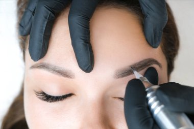 Güzellik uzmanı genç ve güzel bir kadının yüzüne kalıcı kaş makyajı yapar. Kalıcı kaş dövmesi..
