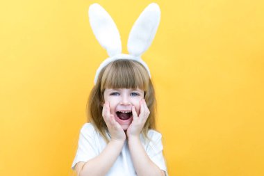 Sarı arka planda tavşan kulaklı neşeli bir kız. Komik, çılgın, mutlu çocuk. Paskalya çocuğu. Paskalya tatili için hazırlık. Promosyon ürünleri. metin ve model için boşluk kopyala