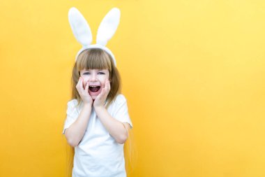 Sarı arka planda tavşan kulaklı neşeli bir kız. Komik, çılgın, mutlu çocuk. Paskalya çocuğu. Paskalya tatili için hazırlık. Promosyon ürünleri. metin ve model için boşluk kopyala
