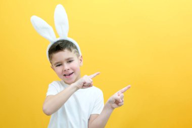 Sarı arka planda tavşan kulaklı neşeli çocuk. Komik mutlu çocuk parmağını boş bir yere doğrultuyor. Metin ve düzen için boşluk kopyala. Paskalya konsepti