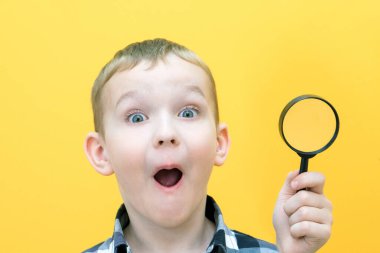 Sıradan giysiler içinde pozitif meraklı bir öğrenci sarı arka plandaki büyüteçten kameraya bakıyor. Sürpriz.