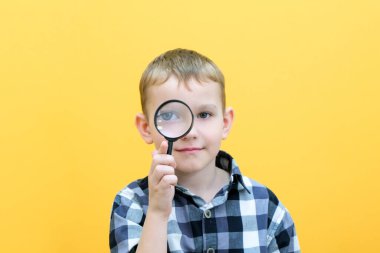 Sıradan giysiler içinde pozitif meraklı bir öğrenci sarı arka plandaki büyüteçten kameraya bakıyor. Sürpriz.