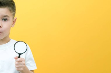 Sıradan giysiler içinde pozitif meraklı bir öğrenci sarı arka plandaki büyüteçten kameraya bakıyor. Sürpriz.