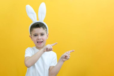 Sarı arka planda tavşan kulaklı neşeli çocuk. Komik mutlu çocuk parmağını boş bir yere doğrultuyor. Metin ve düzen için boşluk kopyala. Paskalya konsepti