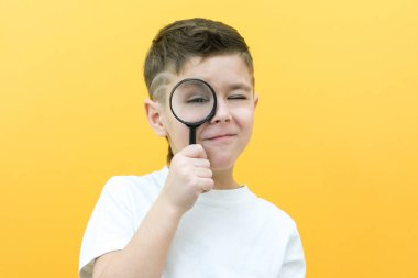 Sıradan giysiler içinde pozitif meraklı bir öğrenci sarı arka plandaki büyüteçten kameraya bakıyor. Sürpriz.