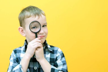 Sıradan giysiler içinde pozitif meraklı bir öğrenci sarı arka plandaki büyüteçten kameraya bakıyor. Sürpriz.