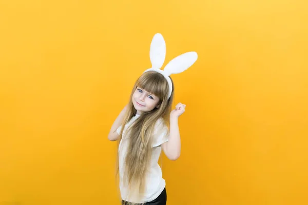 cheerful girl with rabbit ears on her head on a yellow background. Funny crazy happy child. Easter child. Preparation for the Easter holiday. promotional items. copy space for text, mockup