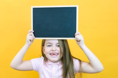 Çarşaf tutan bir kız. Tebeşir tahtası olan şirin küçük bir kız. Sarı arka plan. kopyalama alanı. Metnin için yer