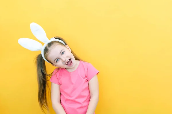 cheerful girl with rabbit ears on her head on a yellow background. Funny crazy happy child. Easter child. Preparation for the Easter holiday. promotional items. copy space for text, mockup