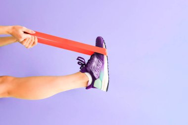 Spor salonu. Fitness bantlarını kullanarak. Eflatun bir arka planda elastik bant ile güzel bacaklar. Eğitim sporu konsepti