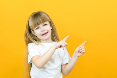 Vay, bak, buraya reklam yap! Arka planda boş bir alanı işaret eden çok tatlı bir kızın portresi, sarı arka planda bir anaokulu kızı.