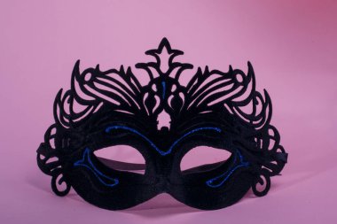 Pembe arka planda parlak mavi çizgileri olan siyah Venedik tarzı karnaval maskesi