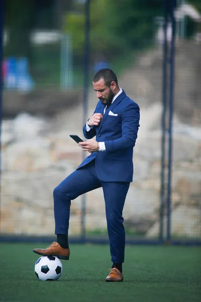 businessman with a ball on his foot chatting with the smartphone inside a soccer field