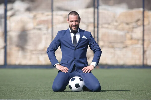 kneeling businessman posing with a ball inside a soccer field