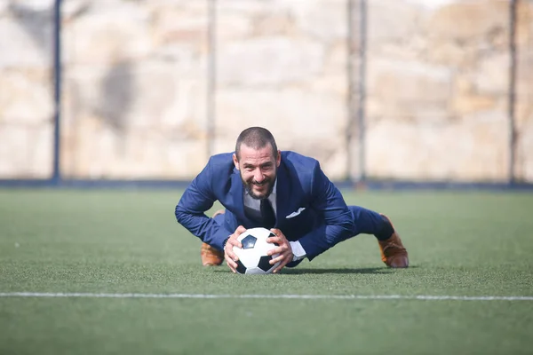flexed businessman leaning on a ball inside a soccer field