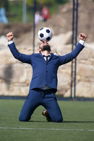 Kafasında top olan bir işadamı futbol sahasındaki golü kutluyor.
